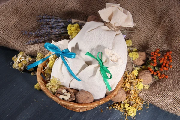 Sachets en textile avec fleurs séchées, herbes et baies sur table en bois, sur fond de sac — Photo