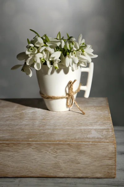 Mooie sneeuwklokjes in cup op grijze achtergrond — Stockfoto