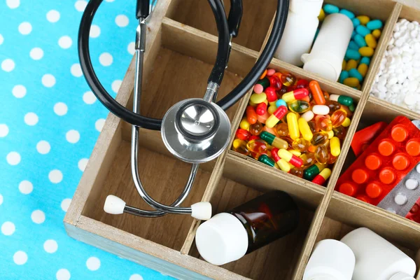 Pilules médicales, stéthoscope, ampoules dans une boîte en bois, sur fond de couleur — Photo