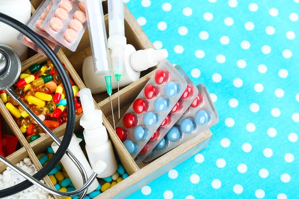 Pilules médicales, stéthoscope, ampoules dans une boîte en bois, sur fond de couleur — Photo