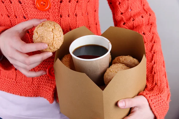 Γυναίκα κρατά το κουτί με τα καφέ και τα cookies σε γκρι φόντο — Φωτογραφία Αρχείου