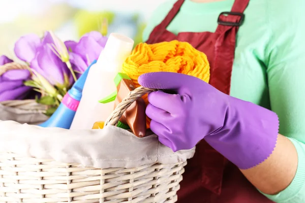 Huisvrouw houden mand met reinigingsapparatuur op lichte achtergrond. conceptuele foto van lente schoonmaak. — Stockfoto