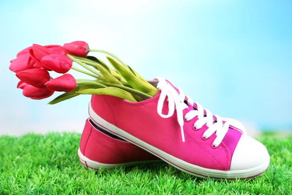 Belle scarpe da ginnastica con fiori all'interno su erba verde, su sfondo luminoso — Foto Stock