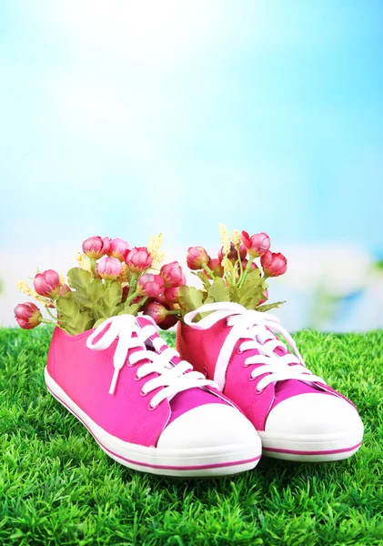 Hermosos zapatos de goma con flores en el interior sobre hierba verde, sobre fondo brillante — Foto de Stock