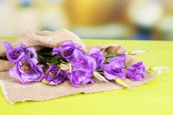 Purple artificial eustoma on sackcloth on color wooden  table, on bright background — Stock Photo, Image