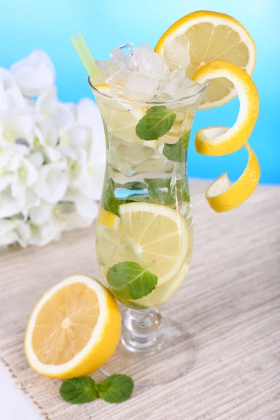 Glass of cocktail with lemon and mint on table on light blue background — Stock Photo, Image