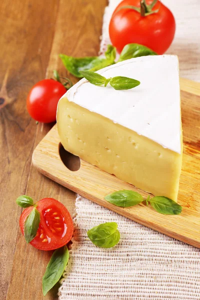 Tasty Camembert cheese with tomatoes and basil, on wooden table — Stock Photo, Image