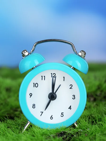 Relógio de alarme azul na grama no fundo natural — Fotografia de Stock