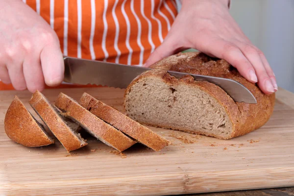 Cutting bread on wooden board on bright background — Stock Photo, Image