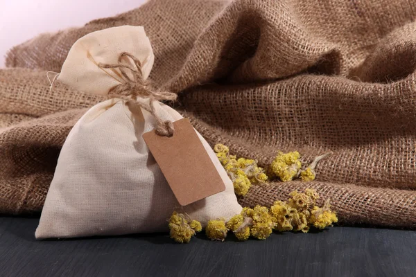 Текстильна сумка з сушеними квітами на дерев'яному столі, на тлі мішковини — стокове фото