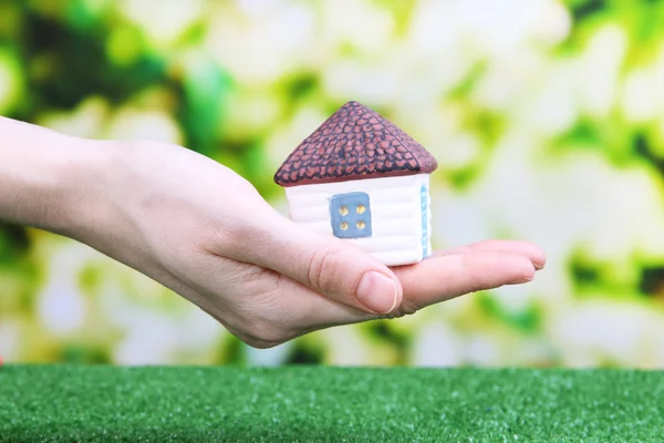 Lille hus i hånden close-up, på grønt græs, på lys baggrund - Stock-foto