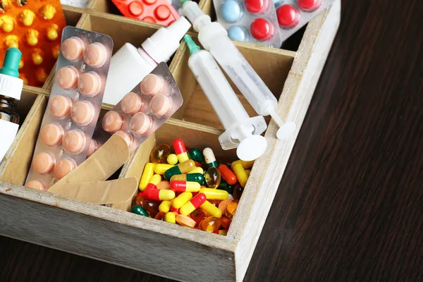 Pilules médicales, ampules dans une boîte en bois, sur fond en bois de couleur — Photo