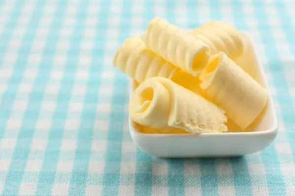 Curls of fresh butter in bowl, on blue tablecloth — Stock Photo, Image