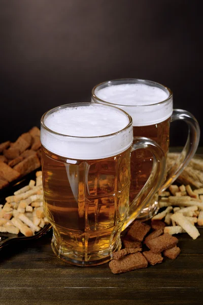 Vasos de cerveza con merienda en la mesa sobre fondo oscuro —  Fotos de Stock