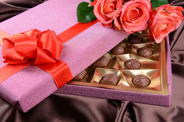 Délicieux chocolats en boîte avec des fleurs sur fond brun — Photo