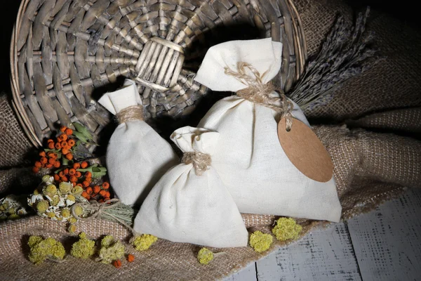 Bolsa de saqueta têxtil com flores secas, ervas e bagas em mesa de madeira, sobre fundo de saco — Fotografia de Stock