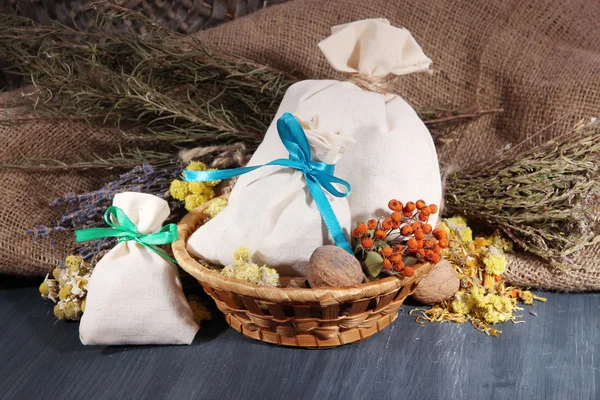 Bustine di tessuto con fiori secchi, erbe e bacche su tavola di legno, su fondo di sacco — Foto Stock