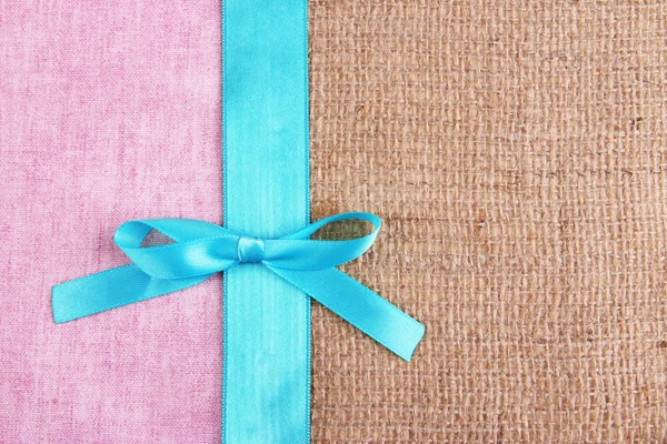 Sackcloth with color ribbon and bow on color fabric background — Stock Photo, Image