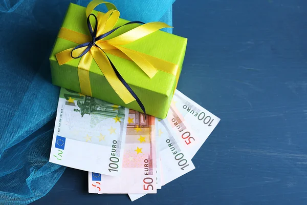 Geschenkbox mit Geld auf farbigem Holzhintergrund — Stockfoto