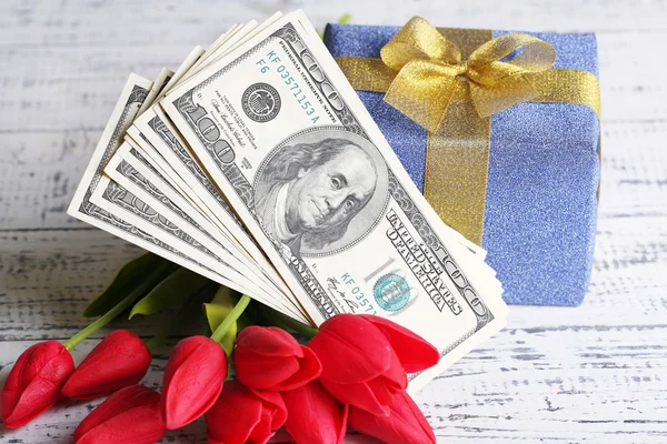 Gift box with money and flowers on color wooden background — Stock Photo, Image