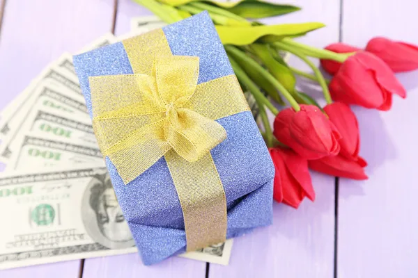 Gift box with money and flowers on color wooden background — Stock Photo, Image