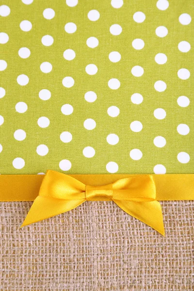 Sackcloth with color ribbon and bow on color fabric background — Stock Photo, Image