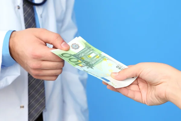 Doctor Masculino recibiendo dinero del paciente, sobre fondo azul — Foto de Stock