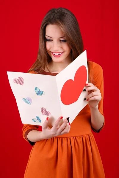 Aantrekkelijke vrouw met briefkaart, op rode achtergrond — Stockfoto