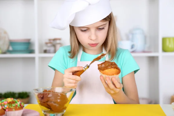 Menina pequena decorando cupcakes na cozinha em casa — Fotografia de Stock