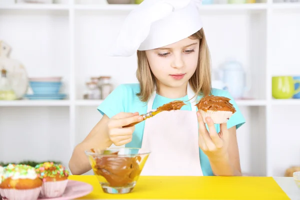 Pieni tyttö koristelu cupcakes keittiössä kotona — kuvapankkivalokuva