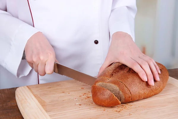 Cutting bread on wooden board on bright background — Stock Photo, Image