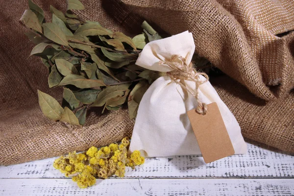 Textile sachet pouch with dried flowers on wooden table, on sackcloth background — Stock Photo, Image