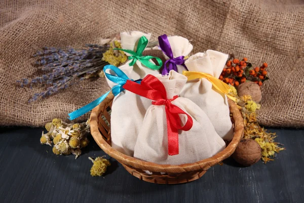 Sachets en textile avec fleurs séchées, herbes et baies sur table en bois, sur fond de sac — Photo