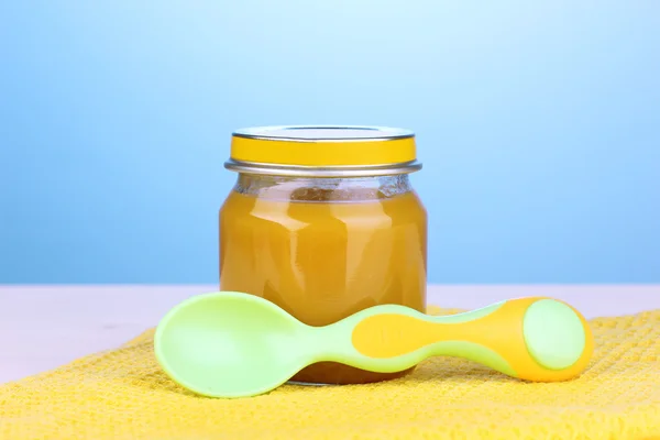 Jar of baby puree with spoon on napkin on blue background — Stock Photo, Image