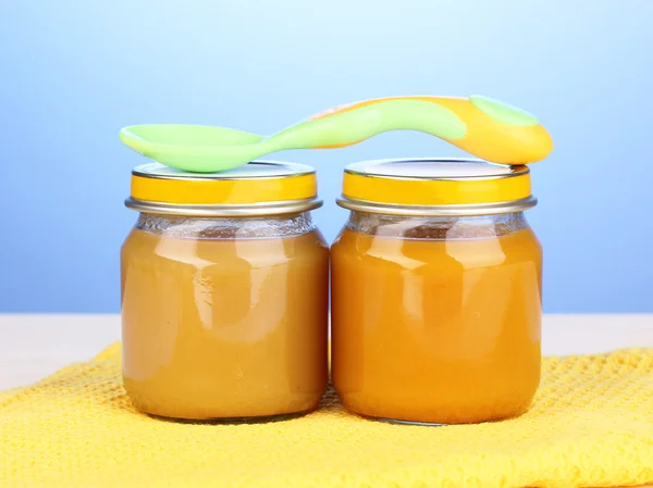 Frascos de puré de bebé con cuchara en servilleta sobre fondo azul — Foto de Stock