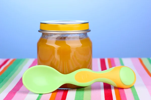 Glas Babypüree mit Löffel auf Serviette auf blauem Hintergrund — Stockfoto