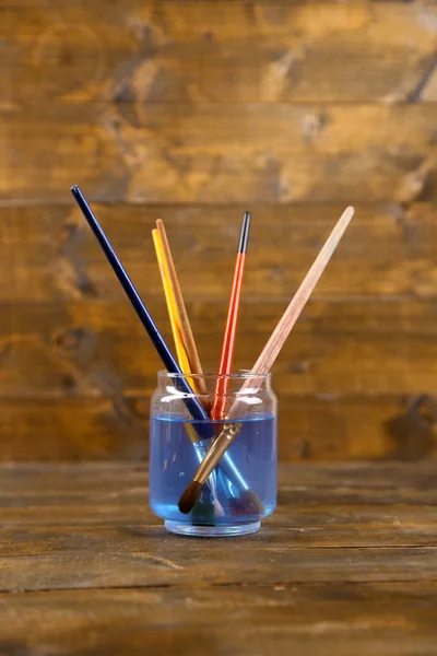 Brushes  in  glass  with water on wooden background — Stock Photo, Image