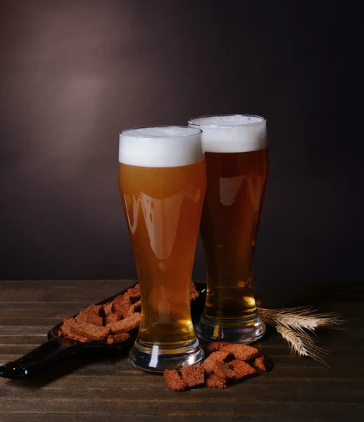 Vasos de cerveza con merienda en la mesa sobre fondo oscuro —  Fotos de Stock