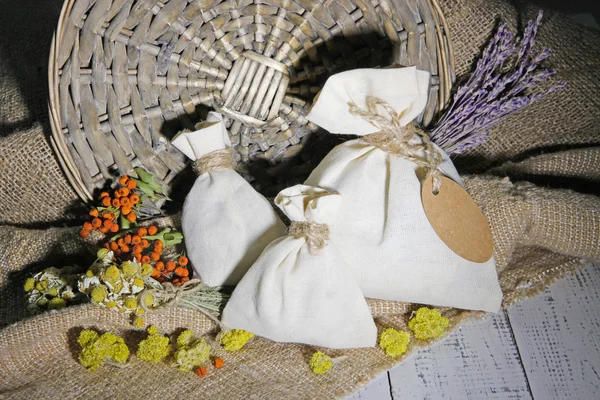 Textile sachet pouch with dried flowers, herbs and berries on wooden table, on sackcloth background — Stock Photo, Image