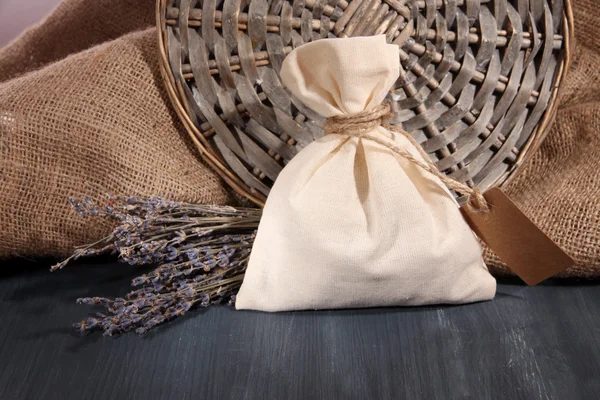 Bustina in tessuto con fiori di lavanda essiccati su tavola di legno, su fondo sacco — Foto Stock