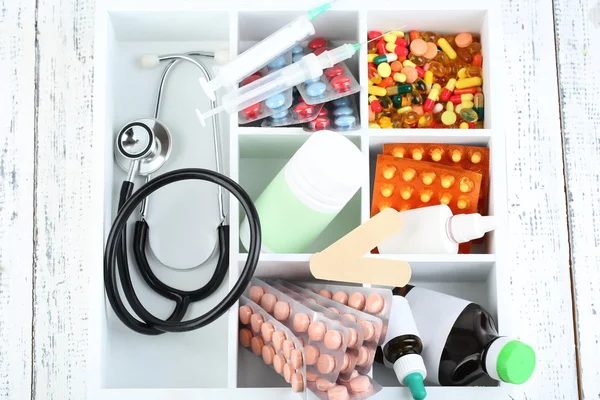 Pastillas médicas, estetoscopio, ampollas en caja de madera, sobre fondo de color — Foto de Stock