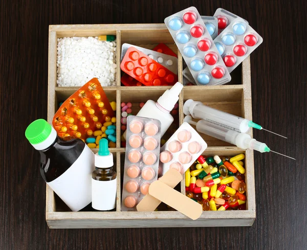 Медицинские таблетки, ампулы в деревянной коробке, на цветном деревянном фоне — стоковое фото