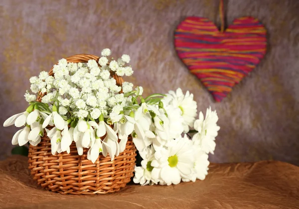 Beautiful snowdrops in basket with heart, on brown background — Stock Photo, Image