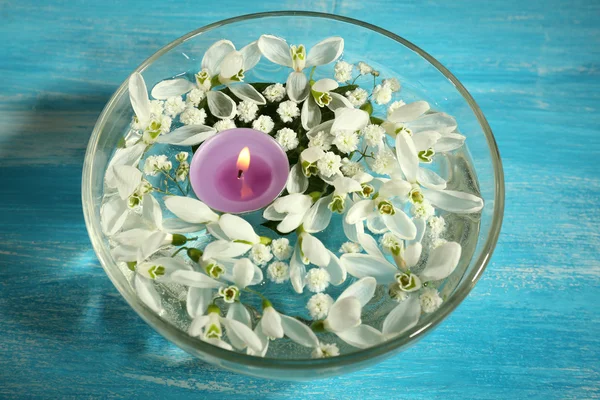 Belles gouttes de neige et bougie dans un bol en verre avec de l'eau, sur fond bleu — Photo