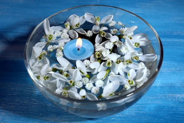 Bellissimi bucaneve e candele in ciotola di vetro con acqua, su sfondo blu — Foto Stock