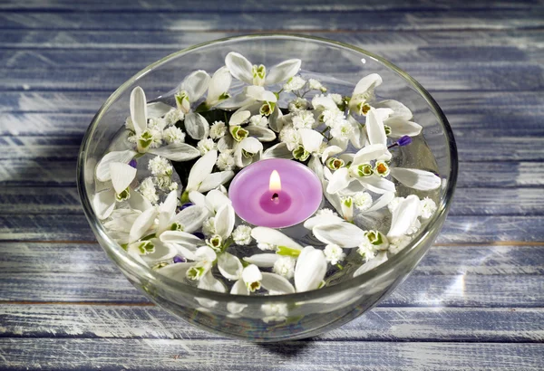 Bellissimi bucaneve e candele in ciotola di vetro con acqua, su fondo di legno — Foto Stock