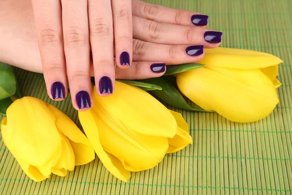 Belles mains de femme avec des fleurs sur fond de bambou — Photo