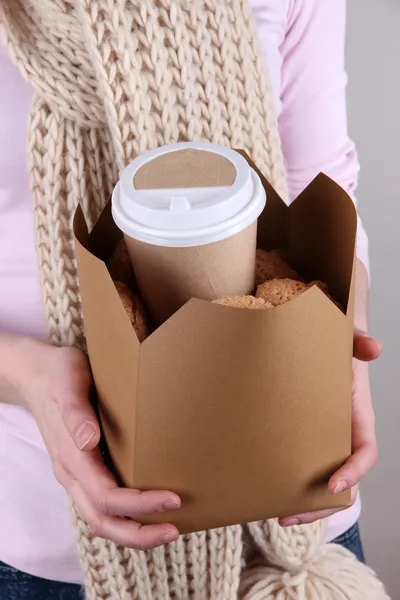 Mulher segura caixa com café e biscoitos em fundo cinza — Fotografia de Stock