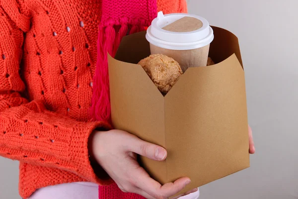 Donna tiene scatola con caffè e biscotti su sfondo grigio — Foto Stock