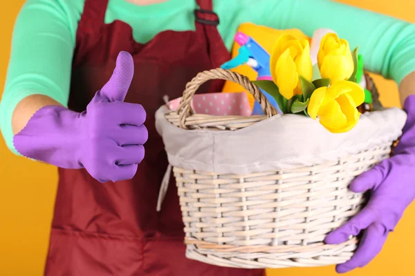 Housewife holding basket with cleaning equipment on color background. Conceptual photo of spring cleaning. — Stock Photo, Image